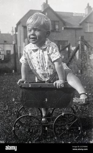 circa1930s-historical-daytime-and-a-little-boy-playing-outside-in-a-garden-climbing-on-top-of-an-old-metal-wheeled-childs-toy-or-dolls-pram-of-the-era-which-has-lost-its-hood-and-handle-an-interesting-object-to-try-and-climb-on-and-the-little-child-shows-good-balance!-2C2YM8W